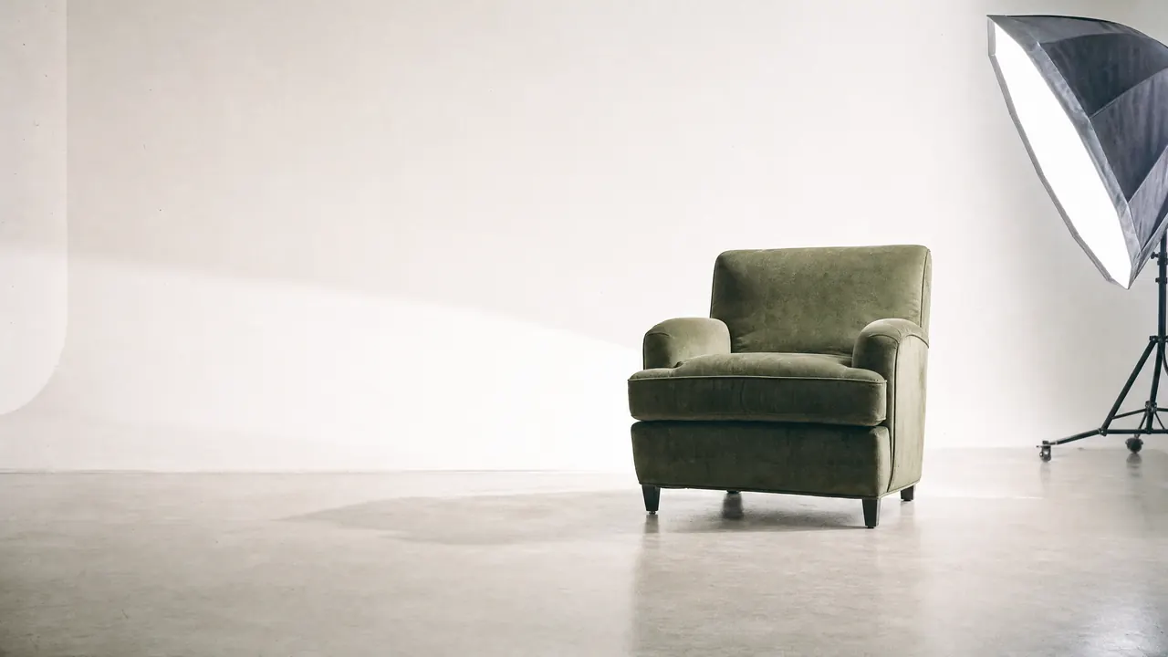An empty sage-green armchair in a studio, lit by one softbox