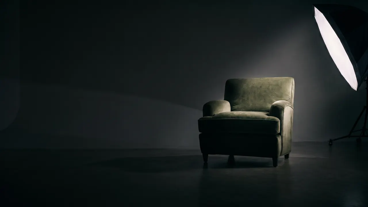 An empty sage-green armchair in a studio, lit by one softbox